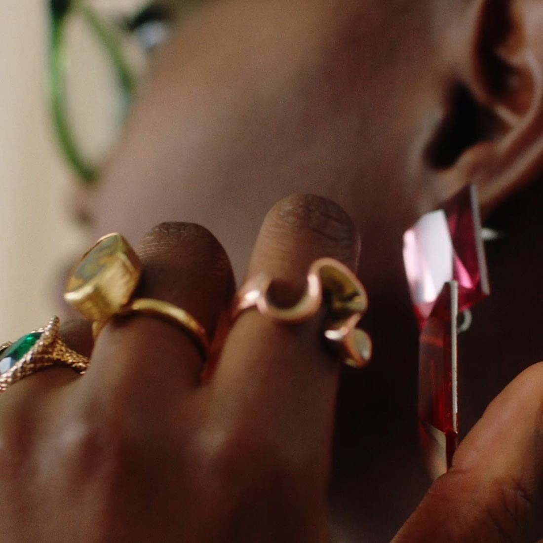 picture depicting a detail of a black woman hand wearing golden rings on each fingers while holding her glossy earring